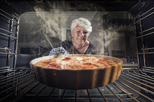 A woman pulling a baked dish from a oven